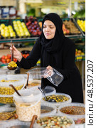 Asian woman in dark blue hijab puts handful of olives in disposable container with ladle. Стоковое фото, фотограф Яков Филимонов / Фотобанк Лори