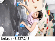 Sporty woman climbing on bouldering wall demonstrating physical strength, technical skill, and determination. Стоковое фото, фотограф Яков Филимонов / Фотобанк Лори