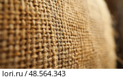 A close-up of burlap fabric reveals its unique texture and weaving patterns, highlighting the natural fibers and warm brown hues. Стоковое AI-изображение, AI-художник Данила Большаков / Фотобанк Лори