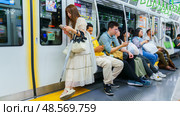 Tokyo, Japan - Sep 30 2024, Panoramic view of male and female passengers standing and sitting in a Tokyo JR subway van, with a girl in a dress standing on a corner, at night Tokyo, Japan. Редакционное фото, фотограф Сергей Богомяко / Фотобанк Лори
