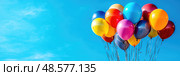 Brightly colored balloons are gently bobbing against a clear blue sky, creating a festive atmosphere during a sunny outdoor gathering. Стоковое AI-изображение, AI-художник Данила Большаков / Фотобанк Лори