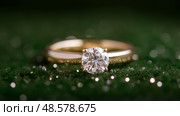 Elegant gold ring featuring a stunning round diamond on a green background. Элегантное золотое кольцо с потрясающим круглым бриллиантом на зеленом фоне. Стоковое AI-изображение, AI-художник Katsiaryna Repich / Фотобанк Лори