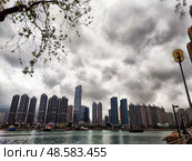 Lantau Island, Hong Kong - April 09, 2024: Dramatic clouds hover above Lantau Island skyline with bustling city life beside serene waters. Стоковое фото, фотограф Кривошеина Елена Леонидовна / Фотобанк Лори