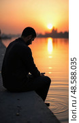 Mourner Whispers Prayers by a River at Twilight, Gazing Into the Water's Reflection; a Moment of Spiritual Reflection. Стоковое AI-изображение, AI-художник Sergey Grishin / Фотобанк Лори