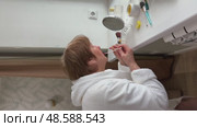 A beautiful senior woman is sitting at home and doing her make-up morning routine. Senior woman putting blush on her face. Стоковое видео, видеограф Ирина Старикова / Фотобанк Лори
