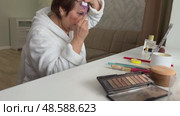 A beautiful senior woman is sitting at home and doing her make-up morning routine. Senior woman putting blush on her face. Стоковое видео, видеограф Ирина Старикова / Фотобанк Лори