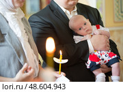 Belarus, Gomel, May 6, 2018. Church of Volotovo. Baptism of a newborn child.The newborn in the arms of the Godfather looks at the candles at the rite of Orthodox baptism. Редакционное фото, фотограф Лазаренко Светлана / Фотобанк Лори
