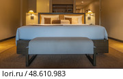 Bedroom interior. The double bed is covered with white sheets. Pillows at the headboard. A banquette. The sconces are lit. Carpet on the parquet floor. Beige shades. Стоковое фото, фотограф Вера Ивановна Кубарева / Фотобанк Лори