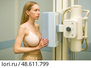 Young woman standing calmly against x ray machine while technician captures chest radiograph for precise medical diagnosis and health screening session. Стоковое AI-изображение, AI-художник Павел Муравьев / Фотобанк Лори