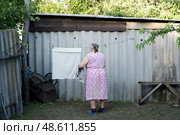 Старая бабушка развешивает белье (2021 год). Редакционное фото, фотограф Татьяна Шестернева / Фотобанк Лори
