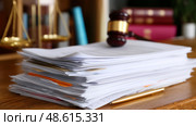 Legal documents stacked on a wooden desk with a gavel and scales of justice in the background. Стоковое AI-изображение, AI-художник Сергей Толмачёв / Фотобанк Лори