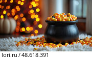 A black cauldron overflows with vibrant candy corn, surrounded by a cozy rug and orange lights, creating a warm and inviting fall atmosphere. Стоковое AI-изображение, AI-художник Данила Большаков / Фотобанк Лори