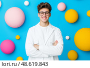 Молодой человек , студент в белом халате, стоит руки скрестив на груди. Яркий голубой фон, парень в очках. Стоковое AI-изображение, AI-художник Никита Мурашов / Фотобанк Лори