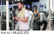 Man with beard trains in the gym and does a triceps exercise in a crossover. Client of a fitness club does a strength training of his arms and pulls the rope handle in the simulator. Стоковое видео, видеограф Яков Филимонов / Фотобанк Лори