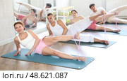 Group of young adults maintaining physical health practicing pilates with elastic band, lying on side and stretching legs at fitness center. Стоковое видео, видеограф Яков Филимонов / Фотобанк Лори