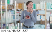 Attentive young female client scrolling phone while looking for something in drugstore. Стоковое видео, видеограф Яков Филимонов / Фотобанк Лори