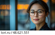 A woman with glasses stands confidently by a window, her fashionable attire complementing the warm city lights in the evening ambiance. Стоковое AI-изображение, AI-художник Данила Большаков / Фотобанк Лори