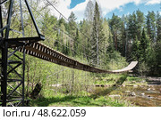 Wooden suspension bridge Humpback in forest over river in spring. Taganay National Park, Russia. Стоковое фото, фотограф Ирина Кононова / Фотобанк Лори