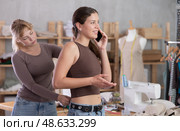 Young tailoress measuring female client speaking on mobile. Стоковое фото, фотограф Яков Филимонов / Фотобанк Лори