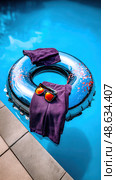 A silver ring floats in a pool with a pair of purple pants and sunglasses. Стоковое AI-изображение, AI-художник Ярославский Максим / Фотобанк Лори