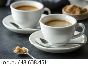 Two Espresso cups with coffee. Freshly brewed espresso shots on a dark wooden table with copy space, background, caffeine. Espresso cups, spoons, saucers. Refreshing hot cup of strong coffee at a cafe. Стоковое AI-изображение, AI-художник Марина Демидюк / Фотобанк Лори
