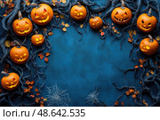 Carved pumpkins with cheerful and spooky faces create a festive Halloween display, enhanced by autumn leaves and spider webs on a blue backdrop. Стоковое AI-изображение, AI-художник Данила Большаков / Фотобанк Лори