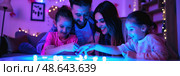 A family gathers around a table playing with glowing toys, enjoying quality time together in a warmly decorated space during the evening. Стоковое AI-изображение, AI-художник Данила Большаков / Фотобанк Лори