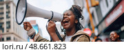 A young activist rallies the crowd, energetically using a megaphone to advocate for change in a lively urban environment. Стоковое AI-изображение, AI-художник Данила Большаков / Фотобанк Лори