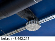 A view of a ventilation system featuring a circular diffuser connected to black ductwork on a bright blue ceiling in a commercial building. Стоковое фото, фотограф Данила Большаков / Фотобанк Лори