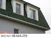 Dormer windows peek out from a distinctive green roof, showcasing architectural styles in a quiet suburban neighborhood with overcast skies. Стоковое фото, фотограф Данила Большаков / Фотобанк Лори