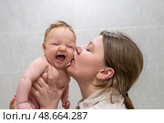 A happy mother kisses her giggling baby in a light-filled room, capturing the joy and bond between them during playtime. Стоковое фото, фотограф Данила Большаков / Фотобанк Лори