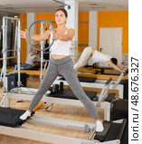 Girl stands on reformer and holds ring, hoop in hands, performs exercises to balance. Стоковое фото, фотограф Яков Филимонов / Фотобанк Лори