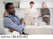 Middle-aged man sitting at the kitchen table with his back to women quarreling to him. Стоковое фото, фотограф Яков Филимонов / Фотобанк Лори