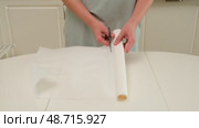 Person cuts a roll of baking parchment paper with scissors on a kitchen table, preparing for cooking or baking tasks. Стоковое видео, видеограф Андрей Журавлев / Фотобанк Лори