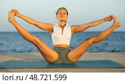 Girl practicing hatha yoga on sea beach, stretching in an asymmetrical seated asana Parivritta Janu Sirsasana. Стоковое фото, фотограф Яков Филимонов / Фотобанк Лори