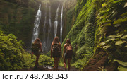 Three adventurers trek through vibrant foliage to unveil breathtaking waterfalls hidden in a lush jungle environment. Стоковое AI-изображение, AI-художник Данила Большаков / Фотобанк Лори