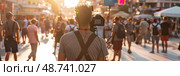 A photographer stands among a crowd, documenting the lively atmosphere in a city as the sun sets, enhancing the scene with warm light. Стоковое AI-изображение, AI-художник Данила Большаков / Фотобанк Лори