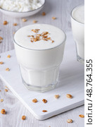 Kefir, buttermilk or yogurt, cottage cheese with granola. Yogurt in glass on white wooden background. Probiotic cold fermented dairy drink. Gut health, fermented products, healthy gut flora conceptt. Стоковое фото, фотограф Наталия Попова / Фотобанк Лори