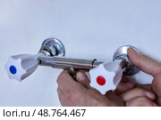 Hands are installing new two handle faucet onto wall outlets, plumber tightens metal fixture with white handles to exposed threaded connectors. Стоковое фото, фотограф Владимир Григорьев / Фотобанк Лори