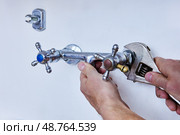 Detaching outdated faucet to install modern fixture, person uses wrench to unscrew metal tap with visible signs of use and colored handle indicators. Стоковое фото, фотограф Владимир Григорьев / Фотобанк Лори