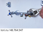 Removing old faucet for replacement with new one, worn metal tap with blue and red handles is being loosened with adjustable wrench on white wall. Стоковое фото, фотограф Владимир Григорьев / Фотобанк Лори
