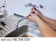 Hands are tightening mounting nut to secure spout on newly installed two handle faucet, plumber ensures firm connection above metal sink. Стоковое фото, фотограф Владимир Григорьев / Фотобанк Лори