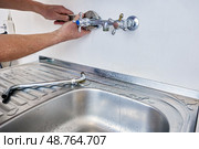 Removing old kitchen faucet for replacement with new one, person uses tools to detach fixture from wall above stainless steel sink. Стоковое фото, фотограф Владимир Григорьев / Фотобанк Лори