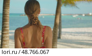 Woman faces sea while walking on sandy beach under palm trees in summer. Стоковое видео, видеограф Ольга Сухарева / Фотобанк Лори
