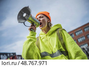 A woman in a yellow jacket is yelling into a megaphone. Стоковое AI-изображение, AI-художник Ярославский Максим / Фотобанк Лори