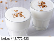 Kefir, buttermilk or yogurt, cottage cheese with granola. Yogurt in glass on white wooden background. Probiotic cold fermented dairy drink. Gut health, fermented products, healthy gut flora conceptt. Стоковое фото, фотограф Наталия Попова / Фотобанк Лори