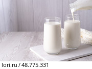 Pouring homemade kefir, buttermilk or yogurt with probiotics. Yogurt flowing from glass bottle on light background. Probiotic cold fermented dairy drink. Trendy food and drink. Copy space. Стоковое фото, фотограф Наталия Попова / Фотобанк Лори