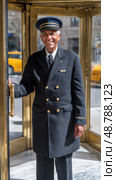 Senior doorman opening revolving door of hotel, welcoming guests. Стоковое AI-изображение, AI-художник Юрий Поздников / Фотобанк Лори