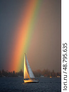 A rainbow is seen above a sailboat on a lake. Стоковое AI-изображение, AI-художник Ярославский Максим / Фотобанк Лори