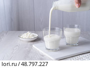 Pouring homemade kefir, buttermilk or yogurt with probiotics. Yogurt flowing from glass bottle on light background. Probiotic cold fermented dairy drink. Trendy food and drink. Copy space. Стоковое фото, фотограф Наталия Попова / Фотобанк Лори